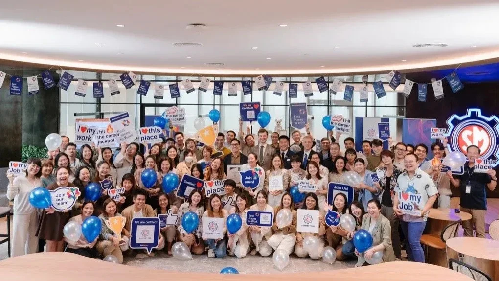 ทีมงานองค์กรถ่ายรูปกลุ่มหลังทำแบบสำรวจความผูกพันพนักงาน พร้อมป้ายรณรงค์วัฒนธรรมองค์กรที่ดี